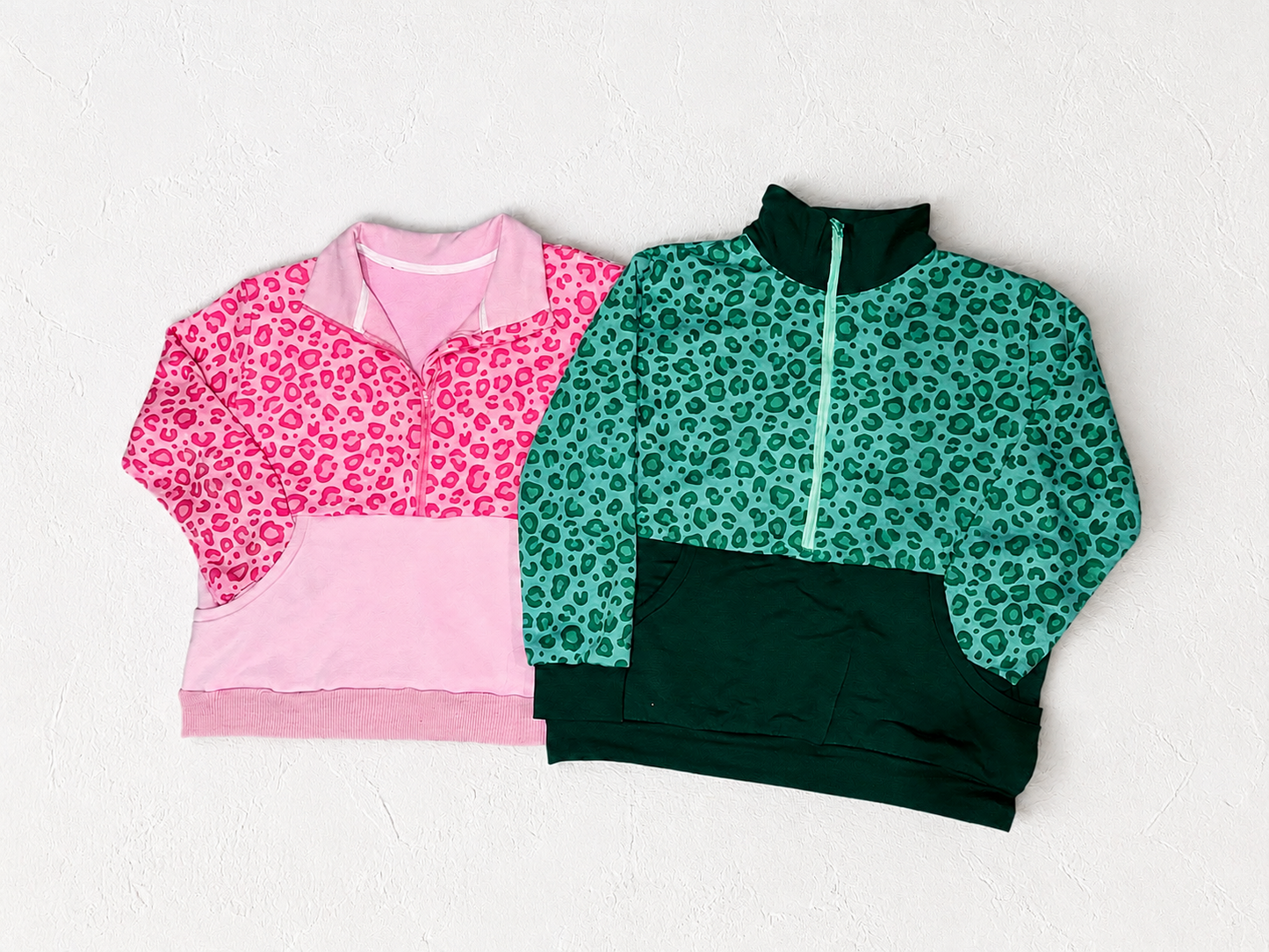 Two leopard print sweatshirts, one pink and one green, on a white textured background.
