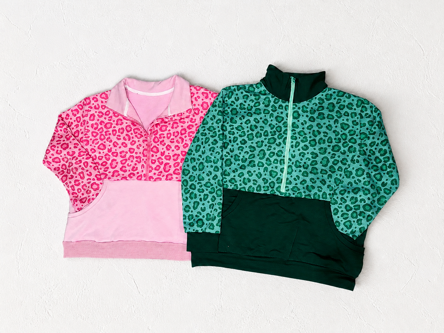 Two leopard print sweatshirts, one pink and one green, on a white textured background.